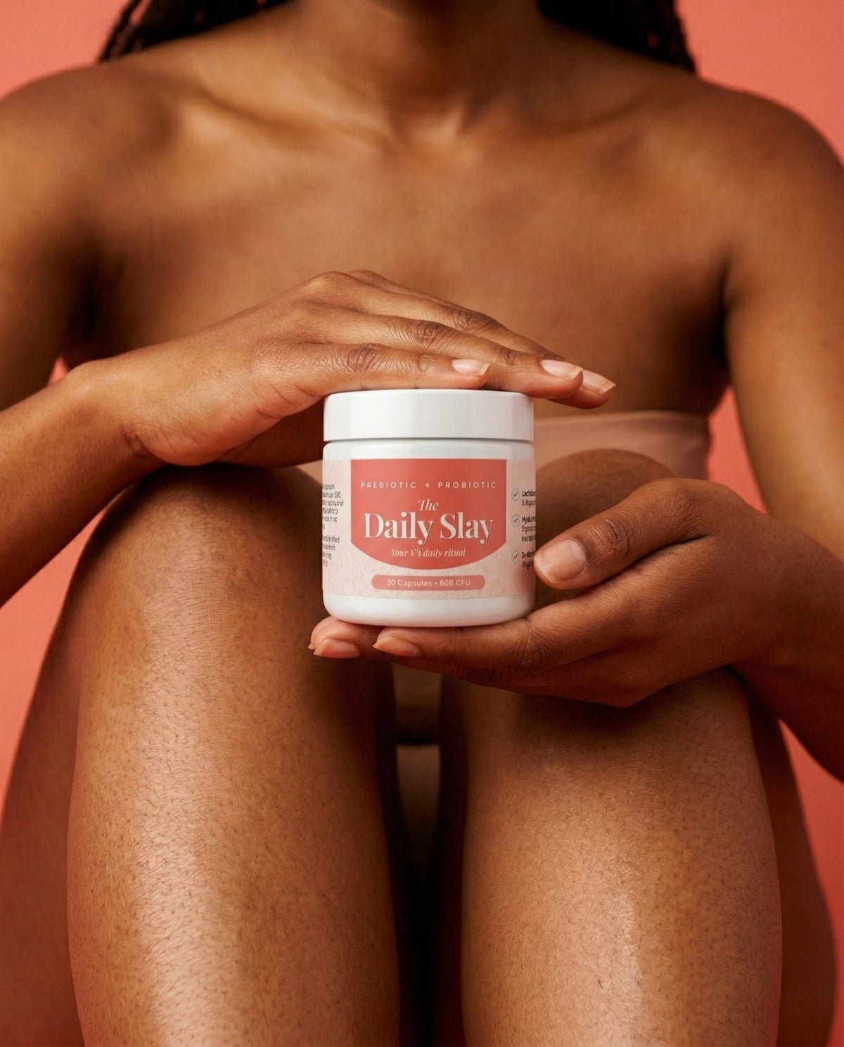 A close-up of a woman holding The Daily Slay jar against her body